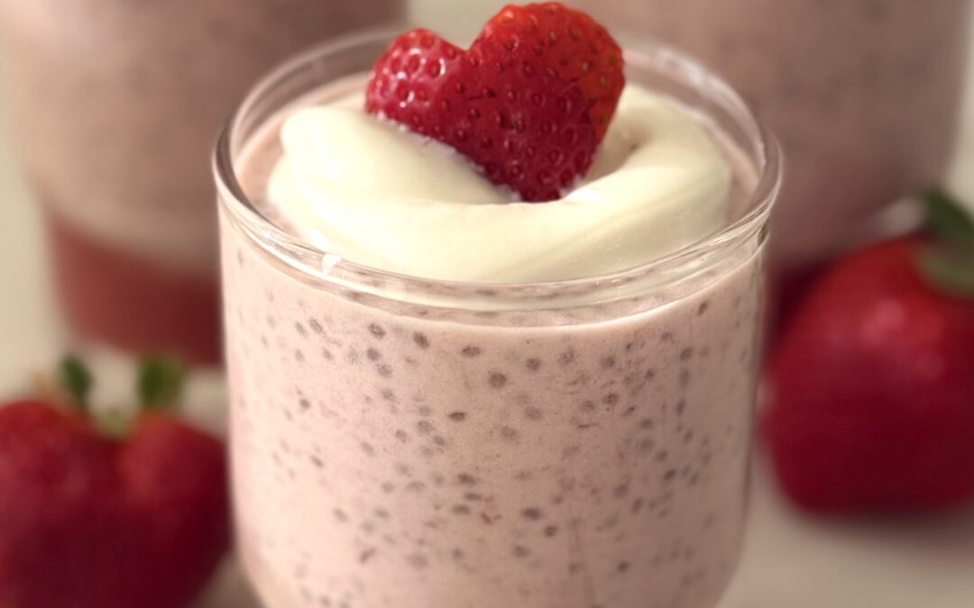 A glass jar holds a Strawberry Chia Seed Pudding with a layer of strawberry puree. The pudding is garnished with a dollop of white yogurt and a heart shaped strawberry slice.