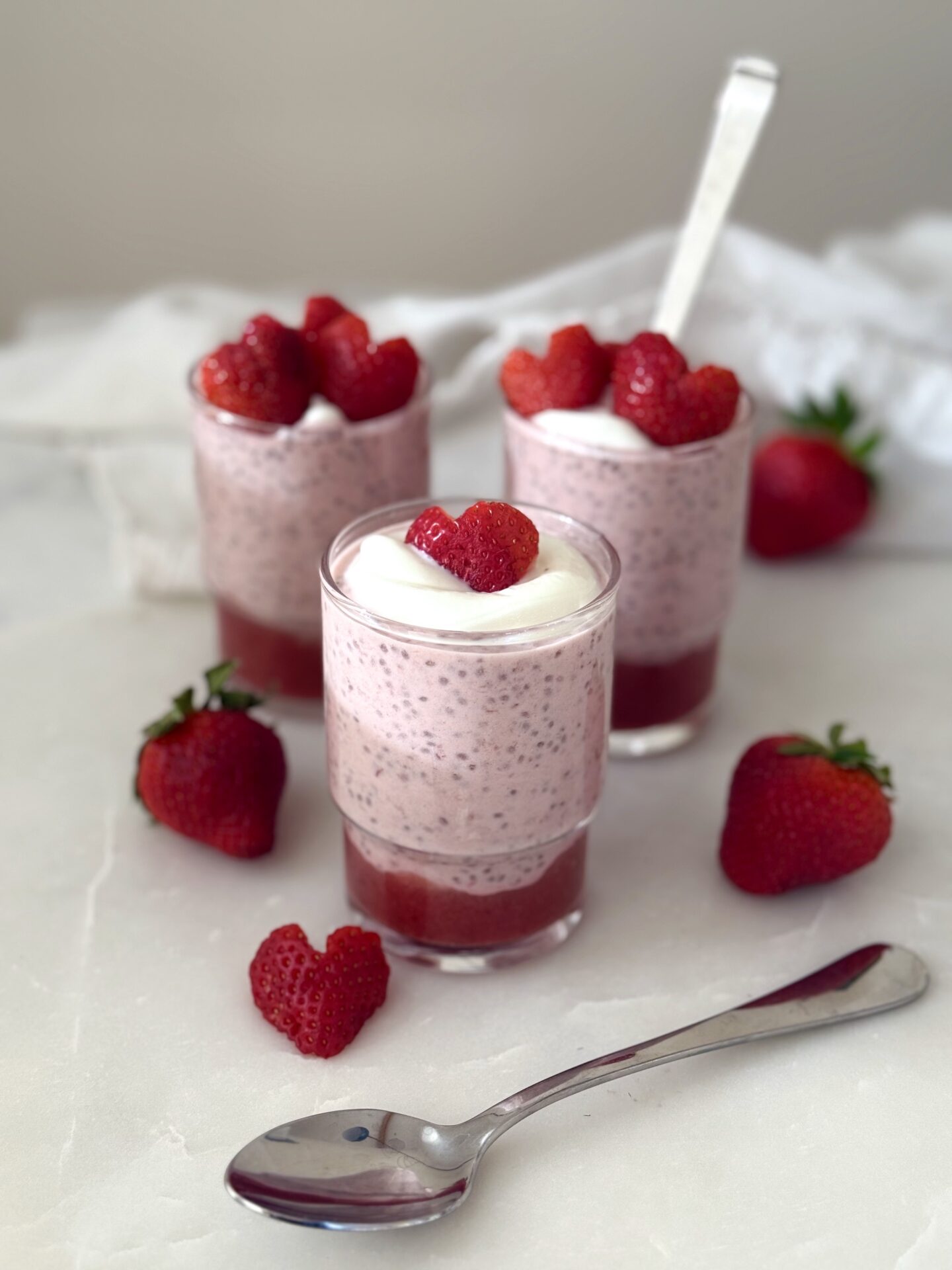 A trio of glass jars hold individual servings of strawberry chia seed pudding.  The puddings are garnished with heart shaped strawberry slices.