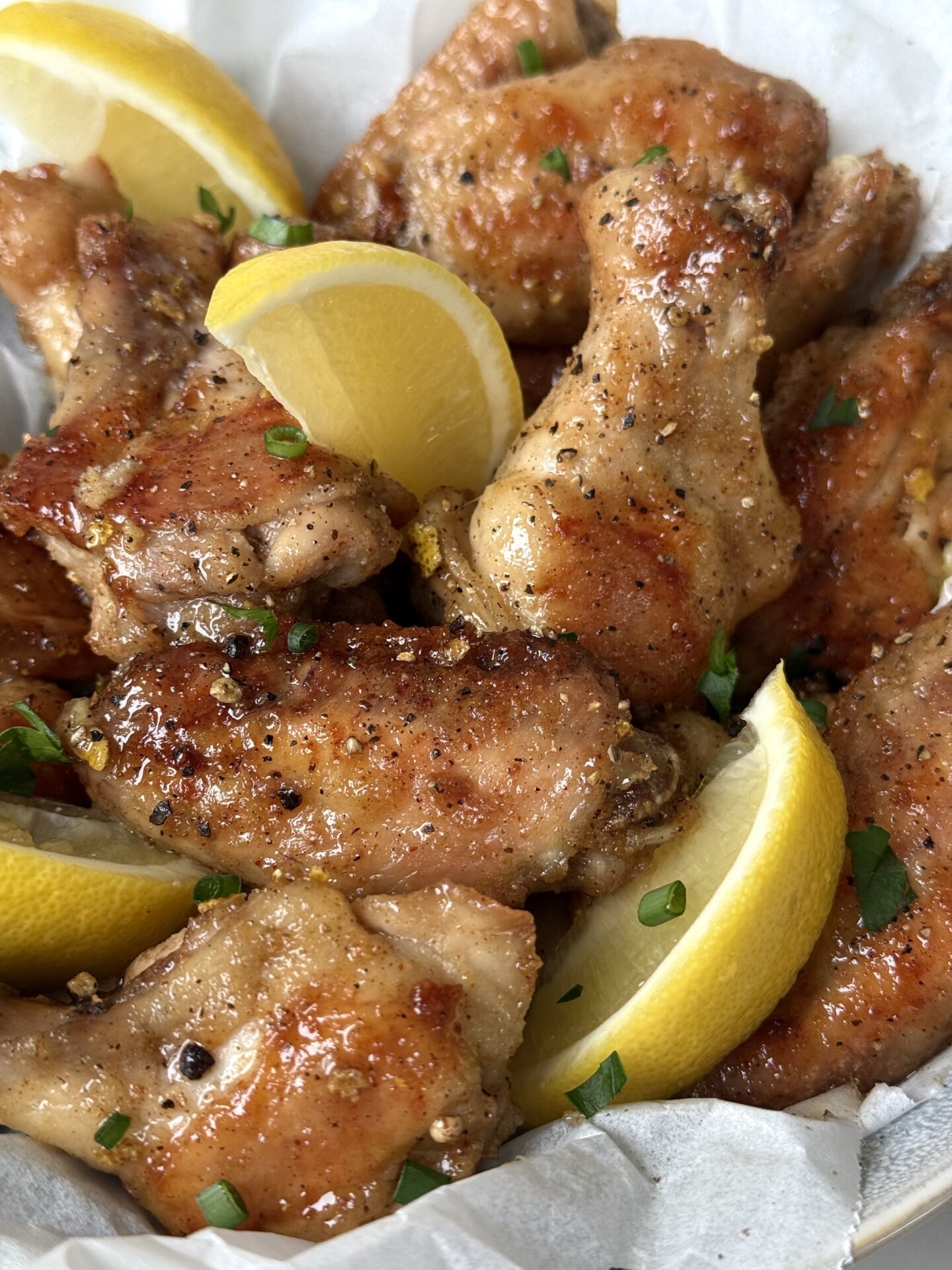 Sweet and Tangy Lemon Pepper Chicken Wings are seen from above, garnished with lemon wedges and fresh parsley and chives