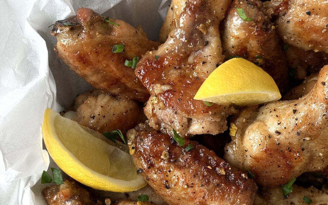 A parchment paper lined bowl of Sweet and Tangy Lemon Pepper Chicken Wings is seen from above, garnished with fresh lemon wedges