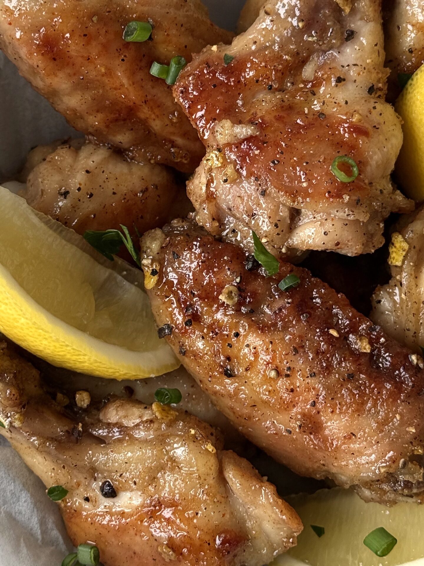 Crisp and golden Lemon Pepper Chicken Wings are seen close up, showing flecks of lemon zest, black pepper and fresh herbs.