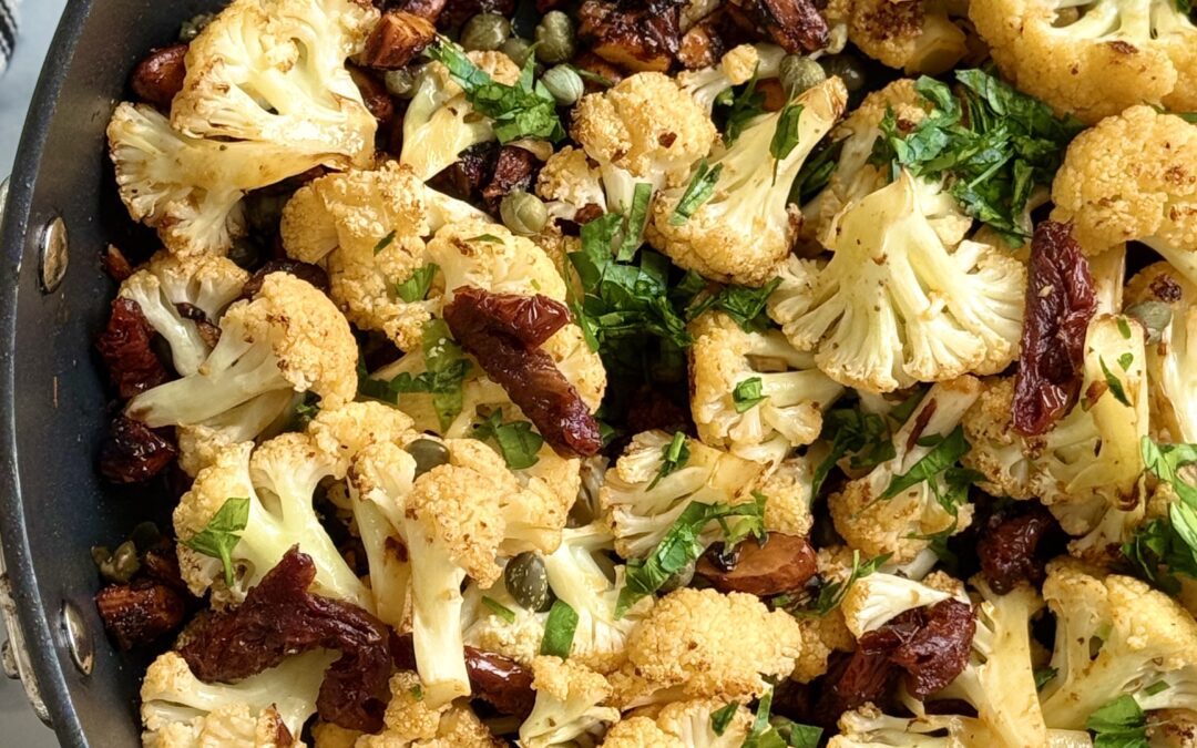 A black pan of Roasted Cauliflower with Sundried Tomatoes, Capers and Crunchy Almonds is seen from above.