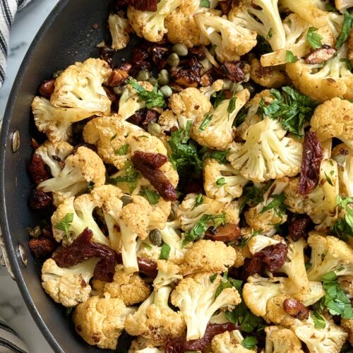 A black pan of Roasted Cauliflower with Sundried Tomatoes, Capers and Crunchy Almonds is seen from above.