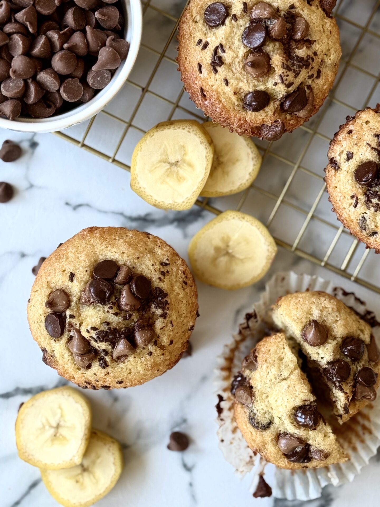 Sour Cream Banana Chocolate Chip Muffins are seen from above, surrounded by banana slices and chocolate chips.