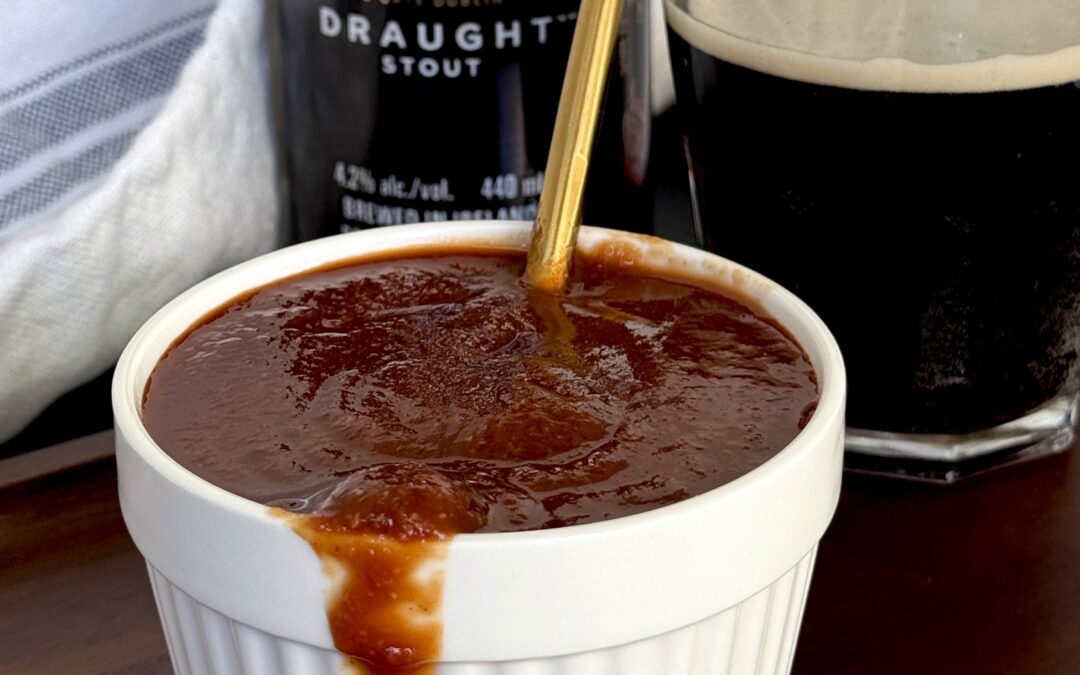 A bowl of Guiness Barbecue Sauce overflows onto a wooden board. A can and glass of Guiness beer can be seen in the background.