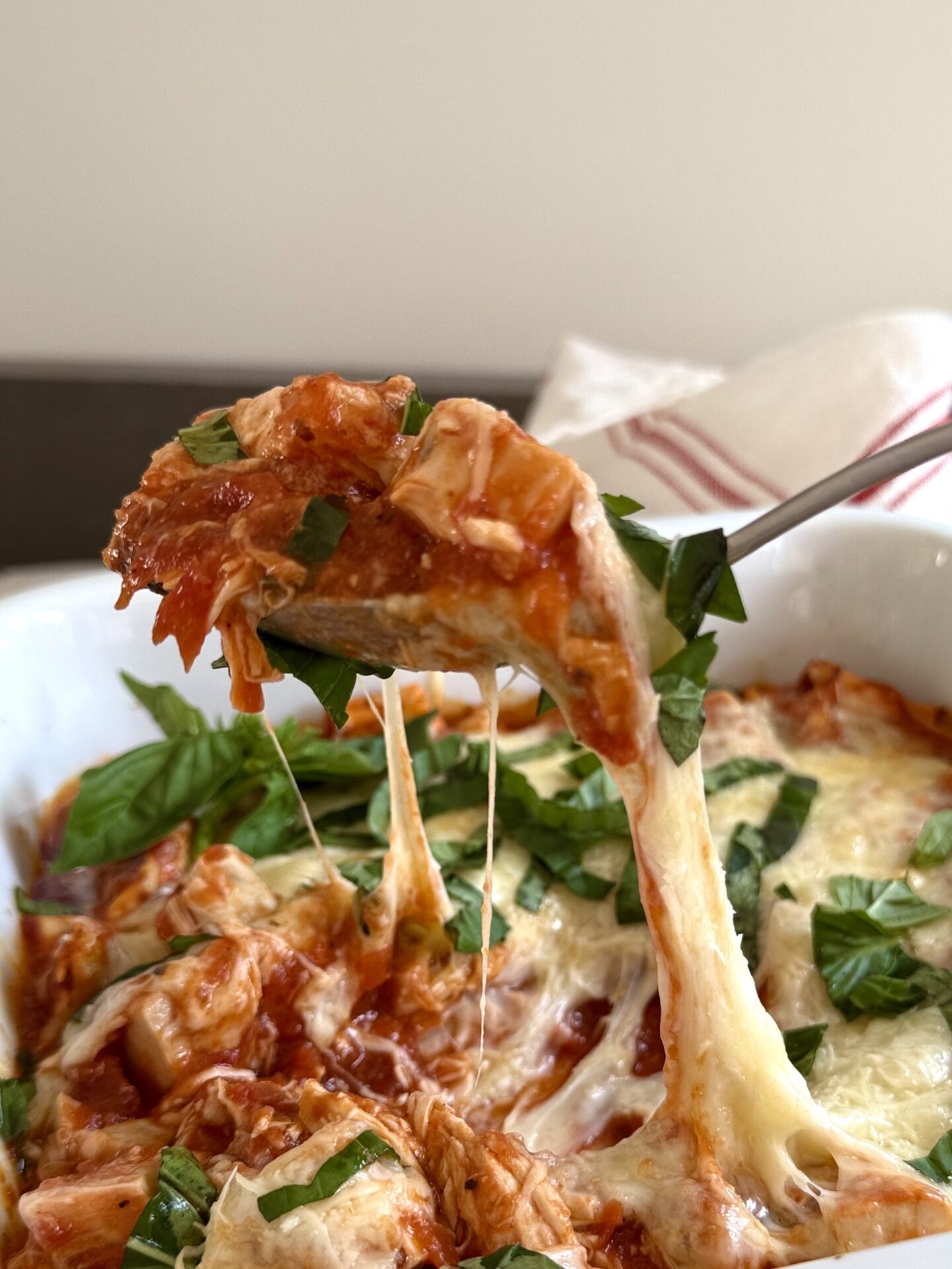 IMG_5263 A large spoon scoops up a hearty portion of Healthier Chicken Parmesan. Melty mozzarella cheese stretches from the casserole to the spoon.