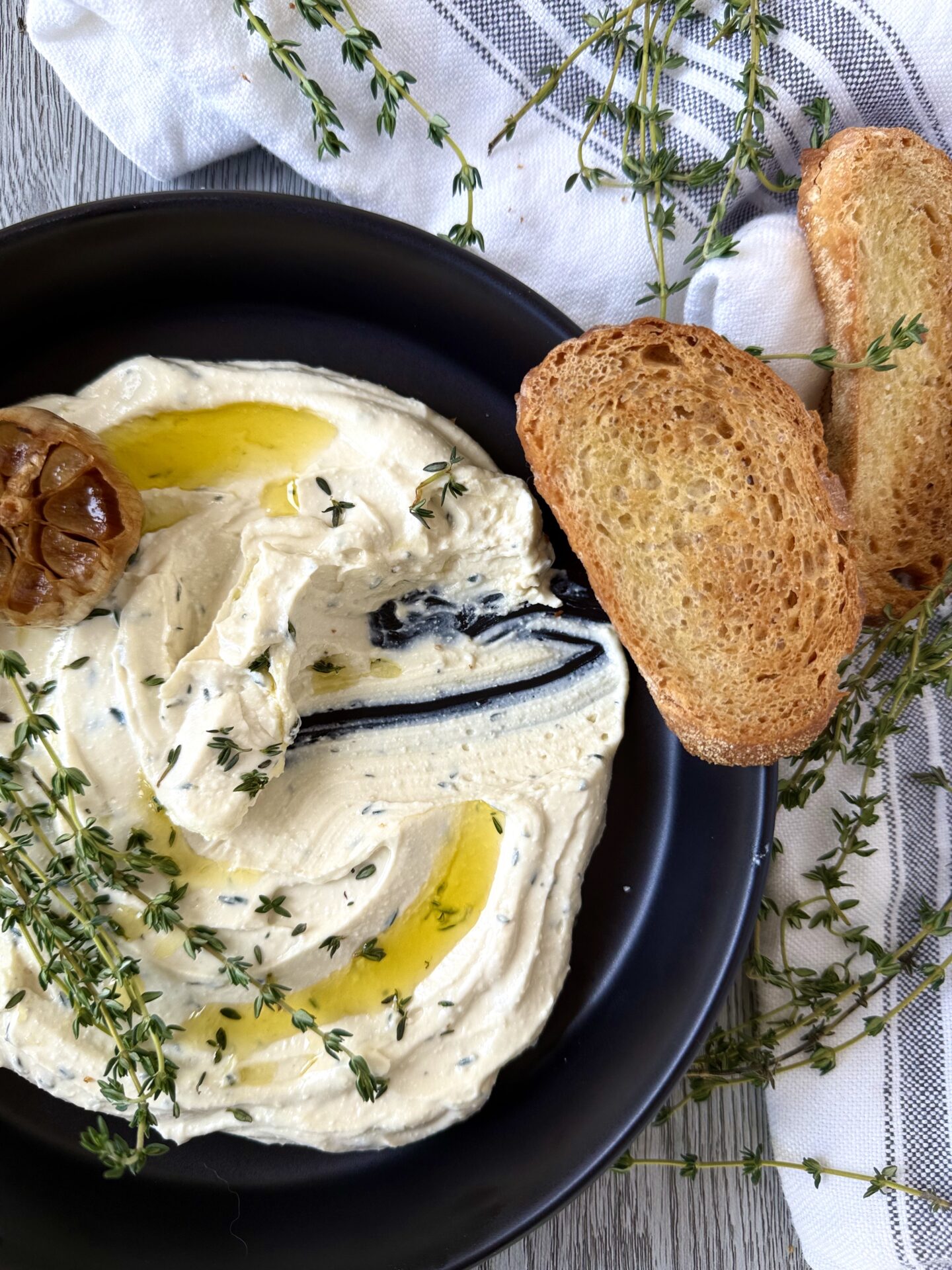 IMG_5639 A bowl of Whipped Feta with Roasted Garlic and Thyme is seen from above. A swoop of dip is missing, implying that someone has used one of the slices of golden toasted baguette to scoop up the dip.